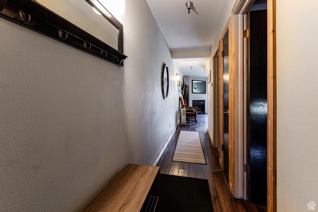 corridor featuring dark wood-type flooring, a textured wall, and baseboards