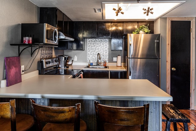 kitchen featuring stainless steel appliances, light countertops, under cabinet range hood, and a sink