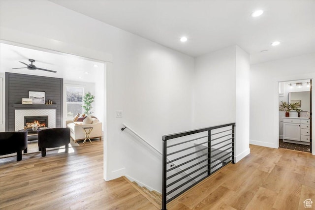 corridor featuring baseboards, an upstairs landing, light wood finished floors, and recessed lighting