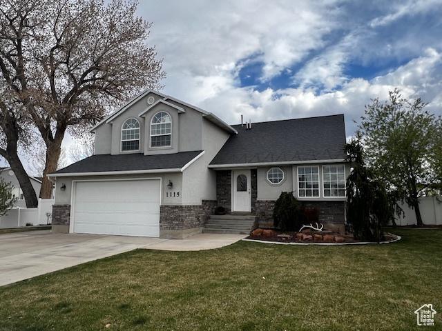 tri-level home featuring stucco siding, an attached garage, a front yard, and concrete driveway