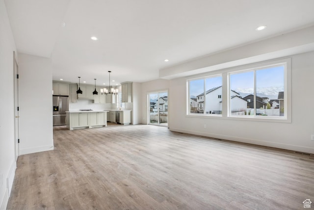 178 N Husker Ln Unit 2, Saratoga Springs, UT 84043 - unfurnished living room featuring light wood finished floors, baseboards, a notable chandelier, and a healthy amount of sunlight