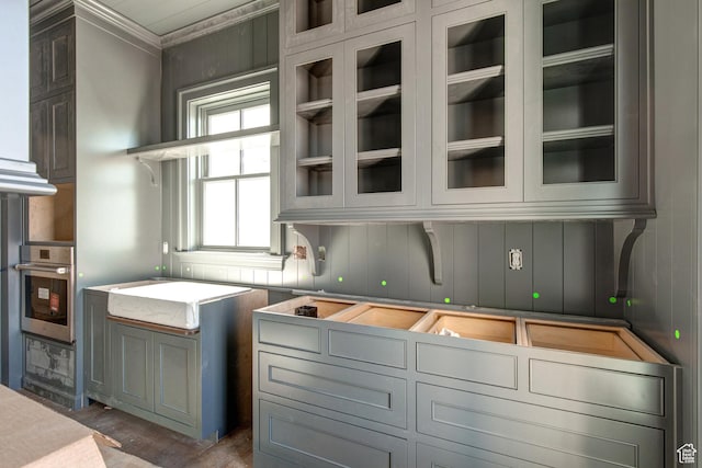 kitchen with light countertops, glass insert cabinets, stainless steel oven, and crown molding