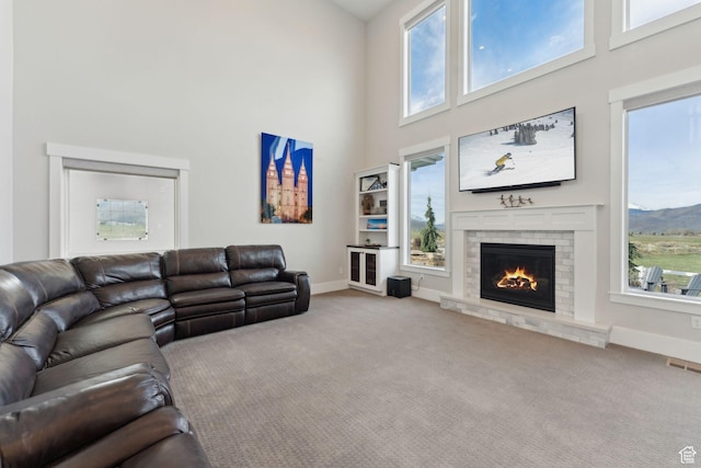 carpeted living room with baseboards, a towering ceiling, visible vents, and a fireplace