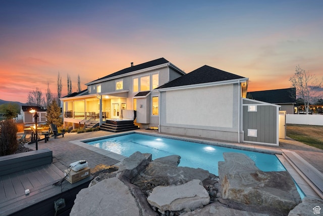 back of property at dusk with a fenced in pool, fence, stucco siding, and a deck