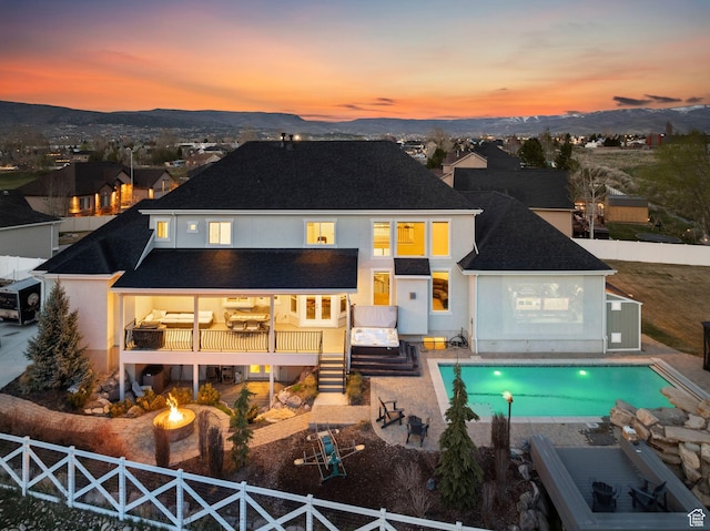 back of property with an outdoor pool, a shingled roof, an outdoor fire pit, a fenced backyard, and stucco siding