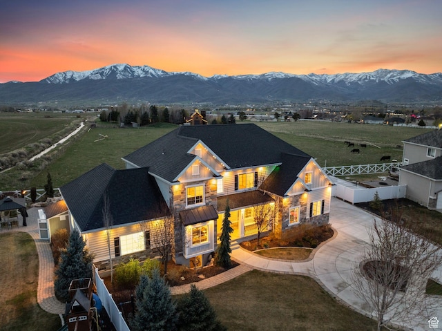 view of front of home with driveway, stone siding, fence, and a mountain view