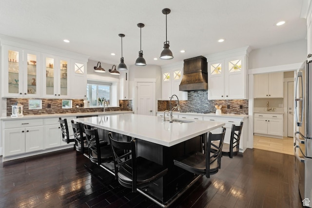 kitchen with a breakfast bar, freestanding refrigerator, a center island with sink, decorative backsplash, and custom exhaust hood