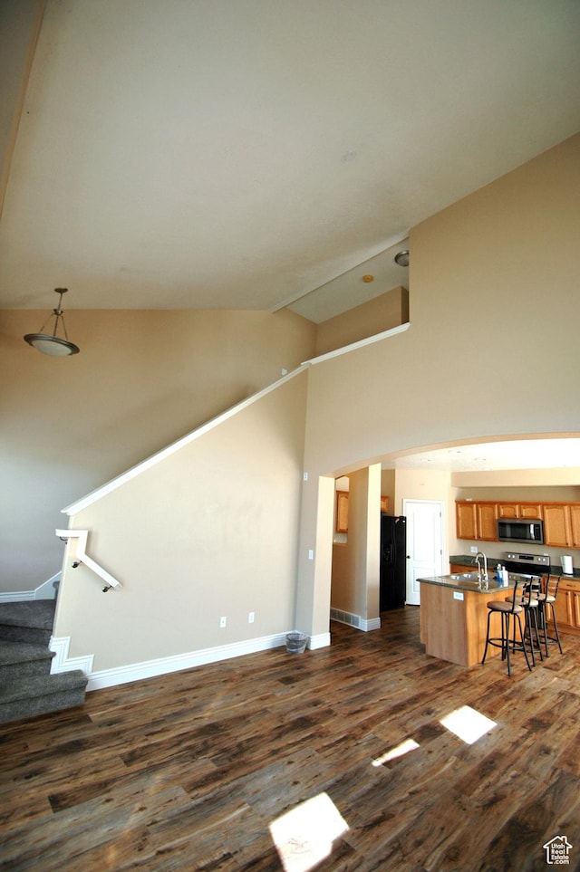 unfurnished living room featuring a sink, high vaulted ceiling, dark wood finished floors, stairway, and baseboards
