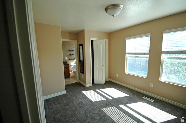 unfurnished bedroom with baseboards, dark carpet, visible vents, and a textured ceiling