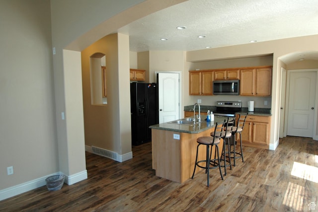 kitchen featuring arched walkways, stainless steel appliances, a sink, and wood finished floors