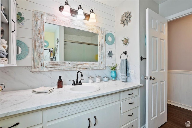 bathroom featuring a wainscoted wall, wooden walls, wood finished floors, vanity, and tasteful backsplash