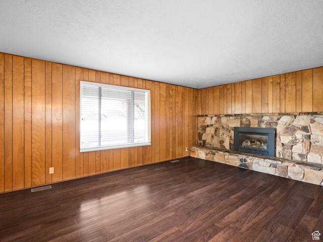 unfurnished living room with a textured ceiling, wood finished floors, visible vents, and a stone fireplace