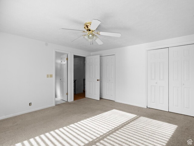 unfurnished bedroom with two closets, ceiling fan, carpet floors, and baseboards