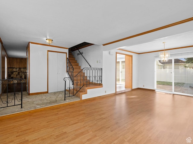 unfurnished living room featuring plenty of natural light, wood finished floors, an inviting chandelier, and crown molding