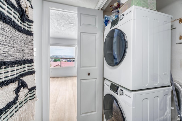 clothes washing area with wood finished floors, stacked washer and dryer, and laundry area