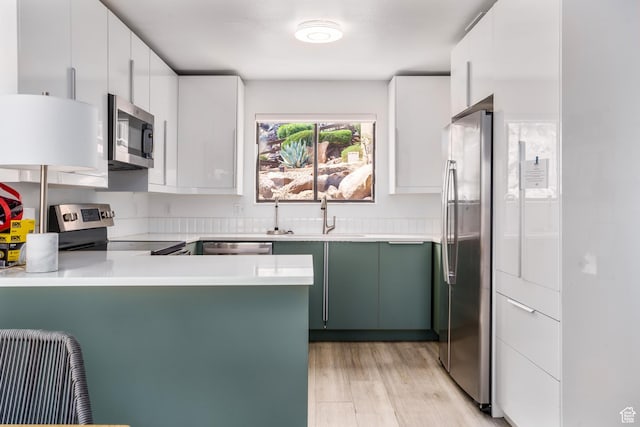 kitchen featuring light wood finished floors, stainless steel appliances, a peninsula, a sink, and light countertops