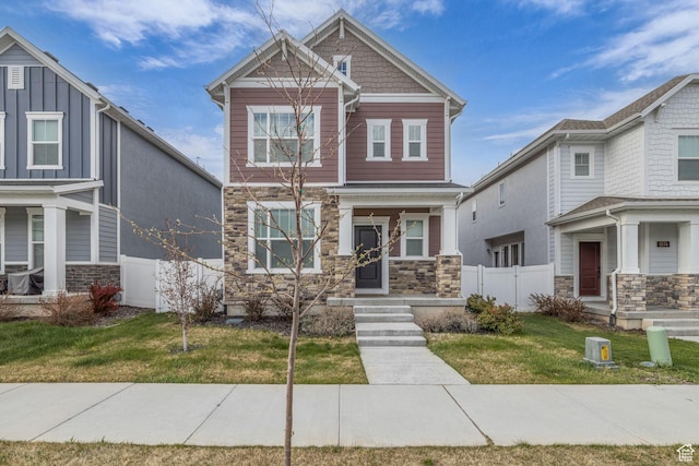 craftsman house featuring stone siding, a front lawn, and fence