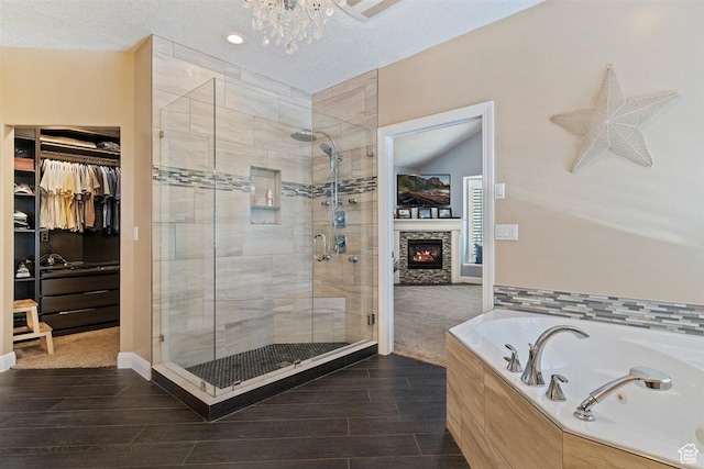 full bath with a textured ceiling, a spacious closet, a garden tub, and a stall shower