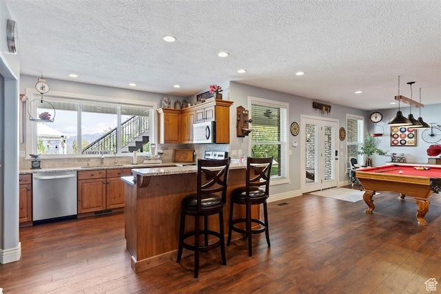kitchen featuring a breakfast bar area, a textured ceiling, pool table, dark wood-type flooring, and stainless steel dishwasher