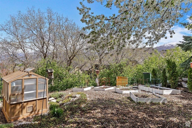 view of yard featuring a greenhouse, a mountain view, an outdoor structure, and a vegetable garden
