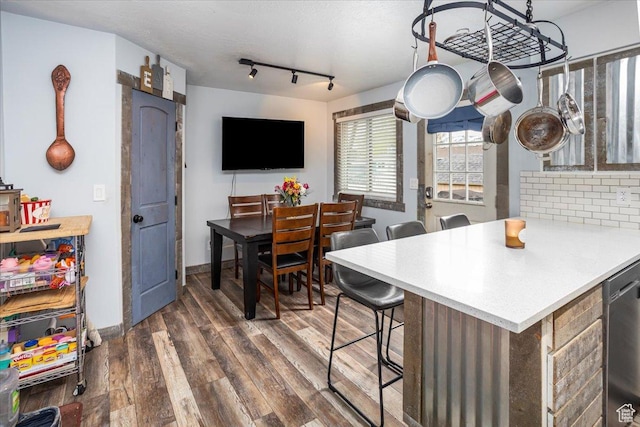 kitchen featuring light countertops, stainless steel dishwasher, dark wood-style flooring, and a breakfast bar area