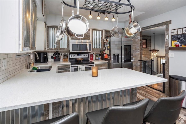 kitchen featuring stainless steel appliances, a peninsula, a sink, light stone countertops, and a breakfast bar area