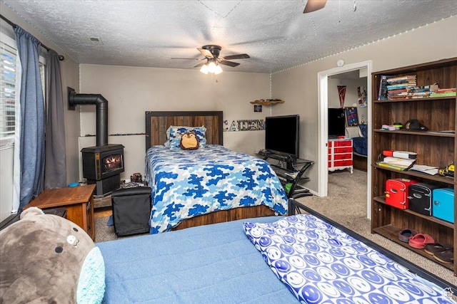 bedroom with ceiling fan, carpet, a textured ceiling, and a wood stove