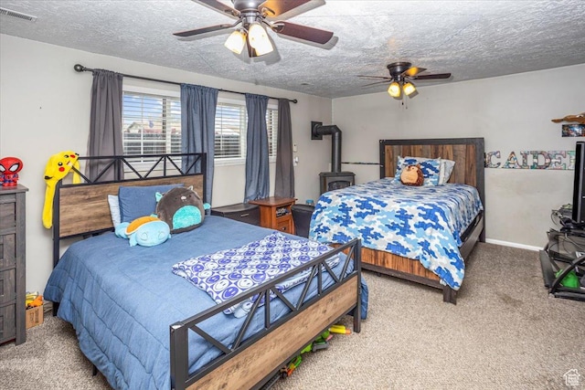 carpeted bedroom with a ceiling fan, a textured ceiling, a wood stove, baseboards, and visible vents