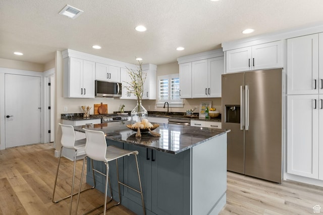 kitchen with a center island, stainless steel appliances, light wood-style flooring, white cabinets, and visible vents