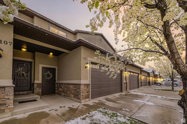 view of front of home with stucco siding, an attached garage, driveway, and stone siding