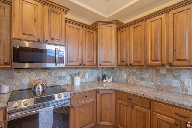 kitchen with appliances with stainless steel finishes, brown cabinetry, backsplash, and light stone counters