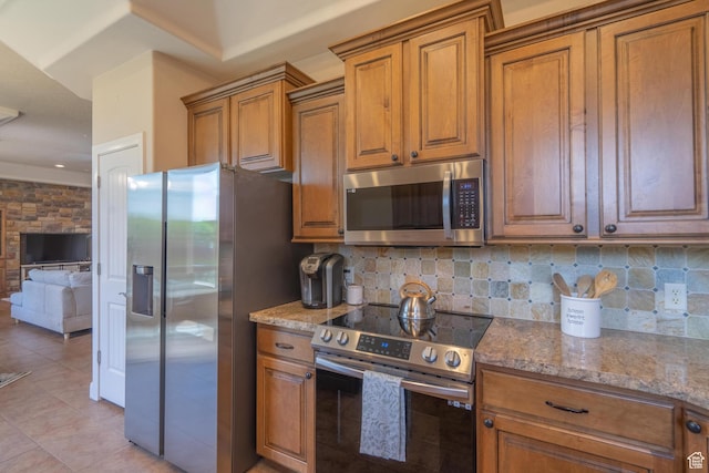 kitchen featuring appliances with stainless steel finishes, brown cabinetry, light stone countertops, and tasteful backsplash