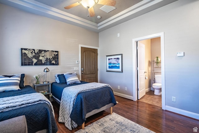 bedroom featuring baseboards, wood finished floors, connected bathroom, a tray ceiling, and ceiling fan