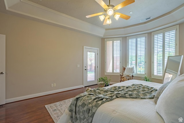 bedroom featuring a tray ceiling, access to exterior, wood finished floors, multiple windows, and ornamental molding