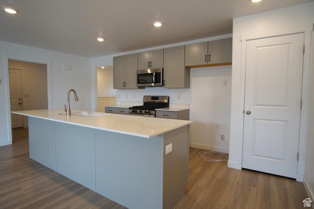 kitchen with stainless steel appliances, a sink, dark wood-type flooring, a center island with sink, and gray cabinetry