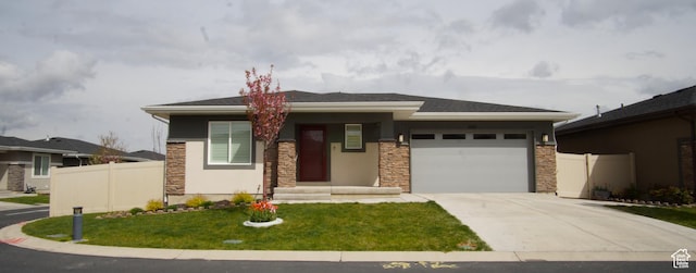 prairie-style home with an attached garage, stone siding, concrete driveway, and fence