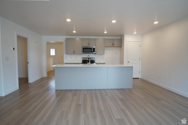 kitchen featuring stainless steel microwave, baseboards, gray cabinetry, and a sink
