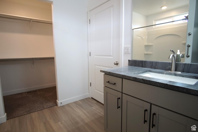 full bath featuring wood finished floors, vanity, a walk in closet, baseboards, and walk in shower