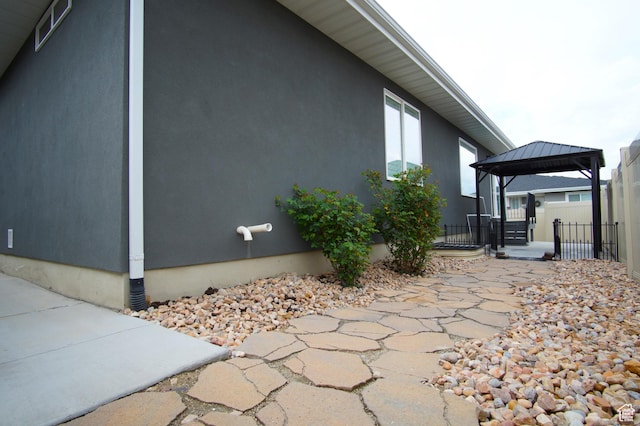 view of home's exterior with stucco siding, a gazebo, fence, and a patio