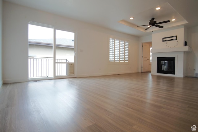 unfurnished living room featuring light wood-style flooring, baseboards, recessed lighting, a ceiling fan, and a raised ceiling