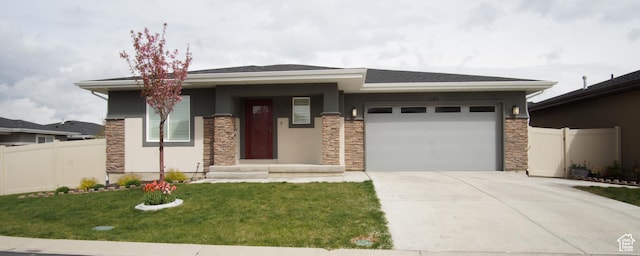prairie-style house featuring concrete driveway, stone siding, an attached garage, fence, and a front yard