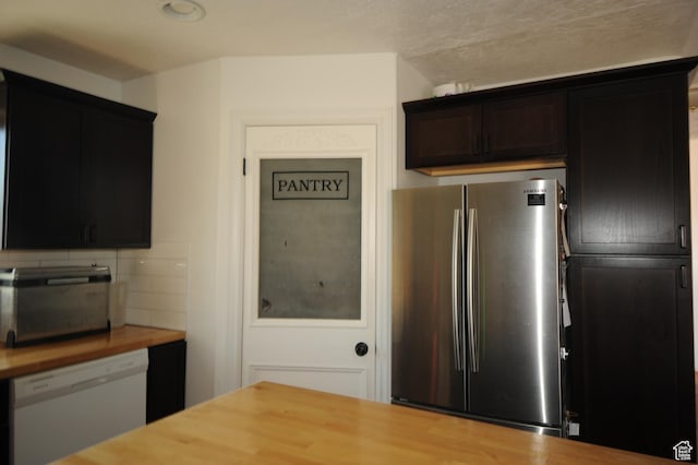 kitchen featuring backsplash, wood counters, white dishwasher, and freestanding refrigerator