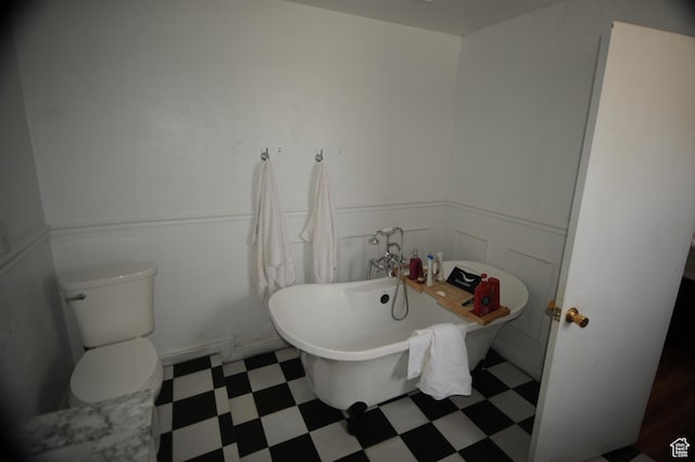 full bath with wainscoting, toilet, a freestanding tub, and tile patterned floors