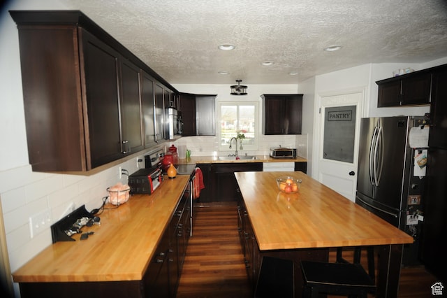 kitchen with stainless steel appliances, decorative backsplash, butcher block countertops, a textured ceiling, and dark wood-style flooring
