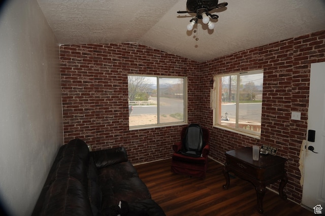 sitting room featuring a textured ceiling, vaulted ceiling, brick wall, wood finished floors, and ceiling fan