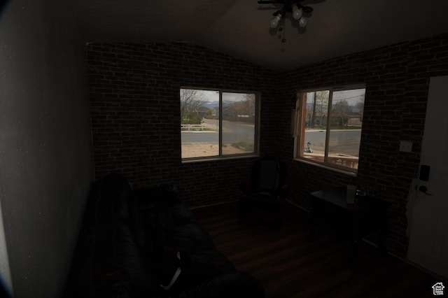 empty room featuring vaulted ceiling, wood finished floors, a ceiling fan, and brick wall