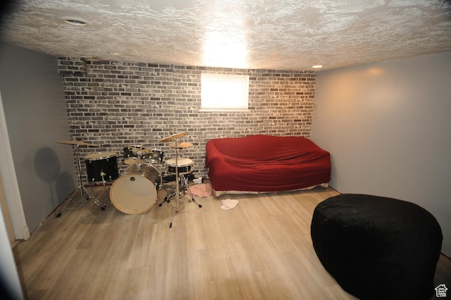 living area with brick wall, wood finished floors, and a textured ceiling