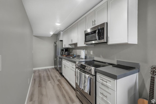 kitchen featuring white cabinets, appliances with stainless steel finishes, a sink, and light wood-style floors