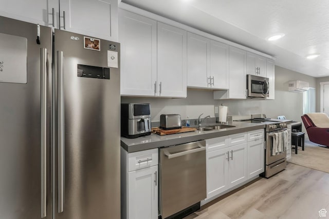 kitchen with light wood-type flooring, dark countertops, a sink, and appliances with stainless steel finishes