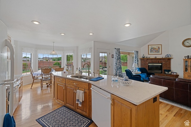 kitchen with light wood finished floors, a sink, a healthy amount of sunlight, white dishwasher, and a fireplace